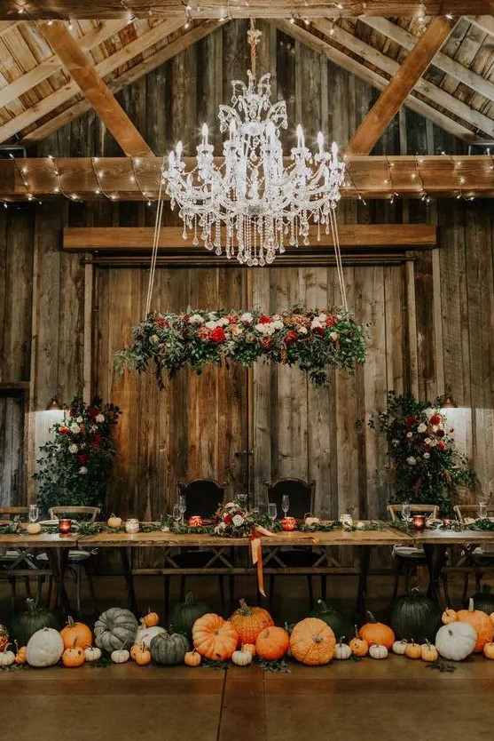 a fantastic fall rustic wedding reception with lots of pumpkins on the floor, bold blooms and neutral ones, greenery and colorful ribbons
