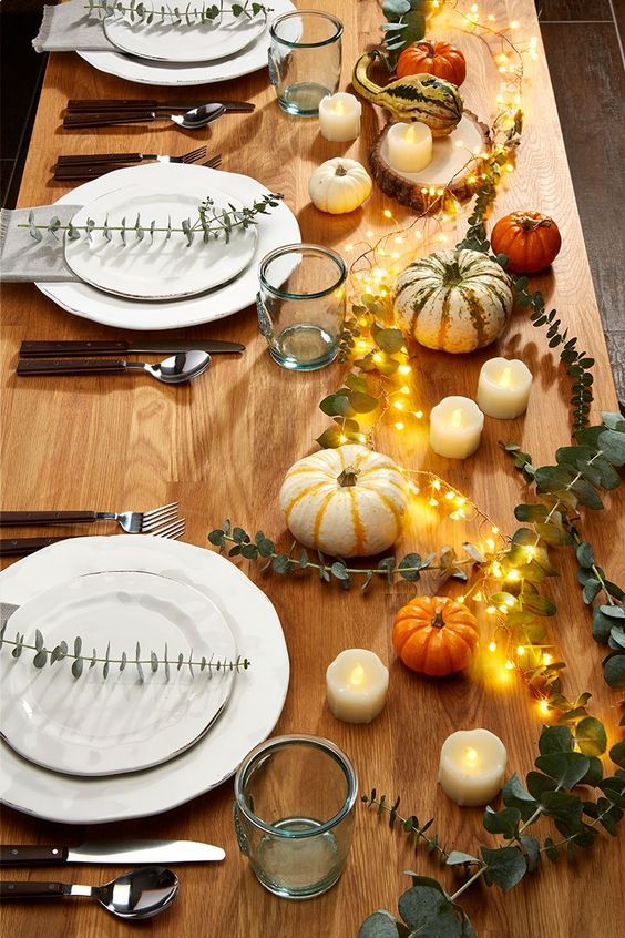 a lovely fall wedding tablescape with pumpkins, lights, white porcelain, modern cutlery and green glasses
