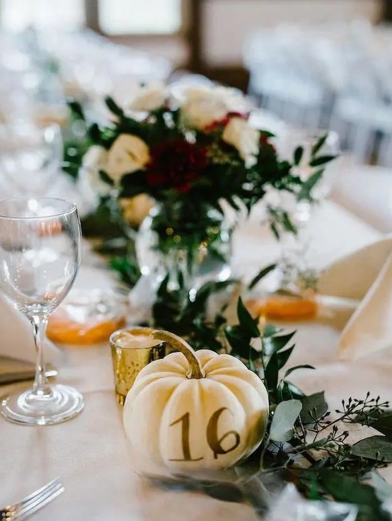 a mini pumpkin with a table number, greenery and candles for fall wedidng table styling