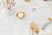 a minimalist neutral wedding table setting with white linens, grey plates and chargers, candles, gold cutlery and dried blooms