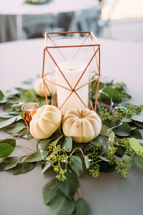 a modern fall wedding centerpiece of greenery, white pumpkins, a geometric candle lantern and lights is easy to repeat yourself