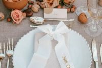 a modern fall wedding tablescape with neutral linens, nuts, pink and peachy roses, pink candles and elegant cutlery
