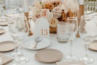a neutral fall wedding table setting with blush and rust flowers, tall and thin candles, grey plates and ribbed glasses