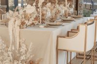 a neutral fall wedding tablescape with neutral candles, neutral dried blooms, grasses and leaves looks ethereal