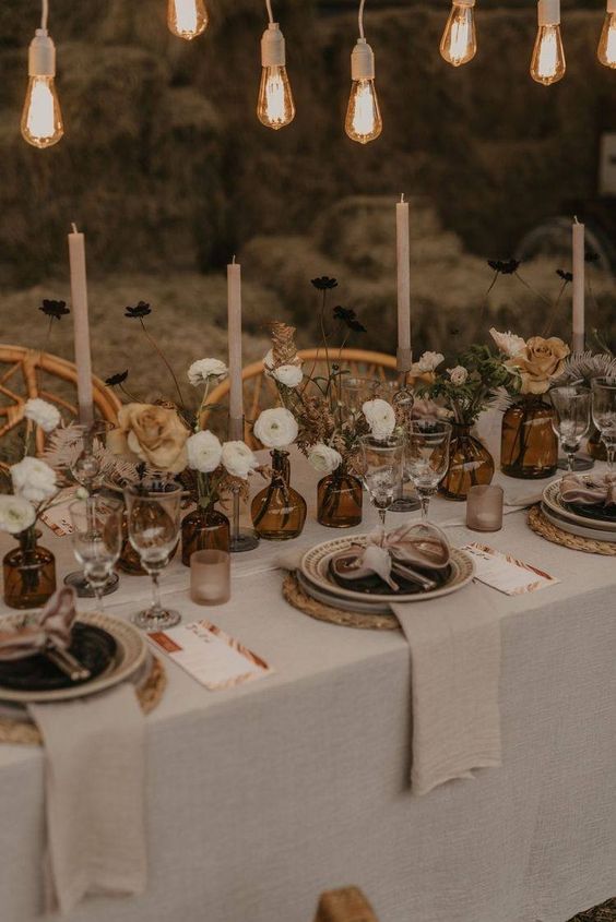 a neutral fall wedding tablescape with neutral flowers, leaves, neutral candles, neutral textiles and bulbs over the table