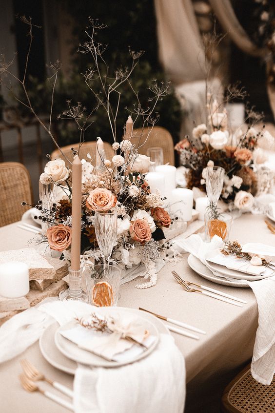a neutral fall wedding tablescape with rust and neutral blooms, dried grasses and berries, neutral linens and candles
