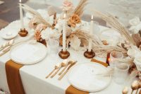 a neutral wedding tablescape with pampas grass and muted color roses, rust napkins and gold cutlery