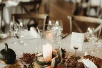 a pretty fall wedding centerpiece of a candle with citrus slices, vine balls, little pumpkins and fall leaves is  a cool idea
