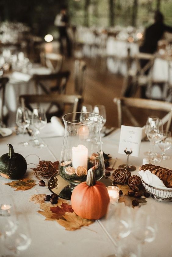 a pretty fall wedding centerpiece of a candle with citrus slices, vine balls, little pumpkins and fall leaves is  a cool idea