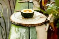 a rustic fall or Thanksgiving tablescape with a green table, wood slices as placemats, greenery and dark glass bottles is very cozy