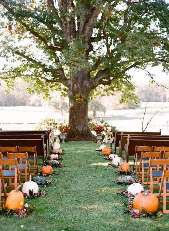 a rustic fall wedding aisle lined up with pumpkins and leaves is a cool and out of the box idea to realize