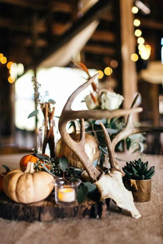 a rustic fall wedding centerpiece of a wood slice, a candle, gilded pumpkins, greenery, a succulent and a skull is a cute idea