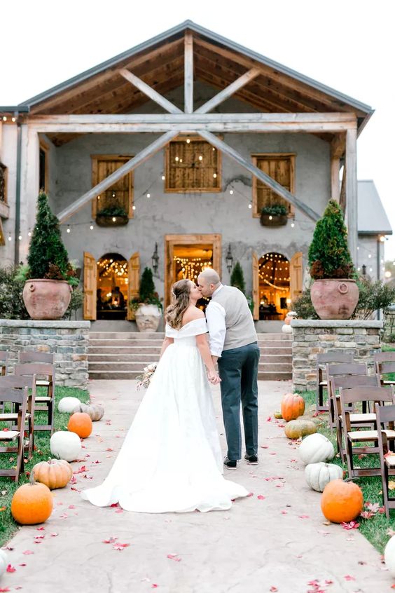 a simple rustic wedding aisle lined up with pumpkins, with bold leaves is a cool idea for a modern rustic space