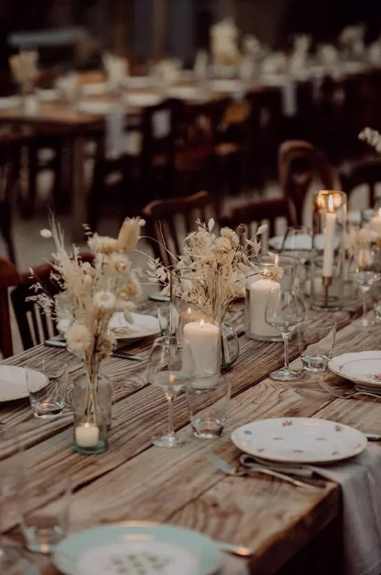 a stylish boho fall wedding tablescape with an uncovered table, dried blooms and grasses and candles plus neutral napkins