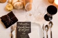 a stylish fall wedding tablescape with white and gilded pumpkins, a reative plate and black and white cards, pillar candles