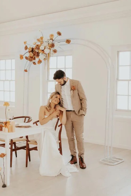 a tan checked pantsuit, a white shirt, brown boots and a bold boutonniere are a cool combo for a boho groom's look