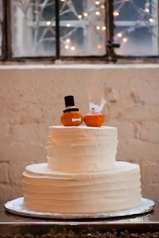 a white buttercream wedding cake topped with two little pumpkins dressed up as the couple is a fun idea