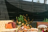 an outdoor fall wedding lounge with amber and brown furniture, a table with blooms, candles and fruit and some bold blooms and heirloom pumpkins on the ground