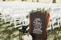 simple backyard fall wedding decor with a chalkboard sign, greenery, dried blooms, pumpkins and a candle lantern