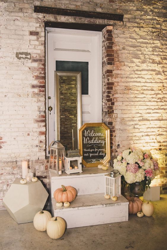 indoor fall wedding decor with neutral pumpkins, neutral blooms, a faceted table with candles and candle lanterns