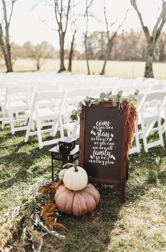 simple backyard fall wedding decor with a chalkbaord sign, greenery, dried blooms, pumpkins and a candle lantern