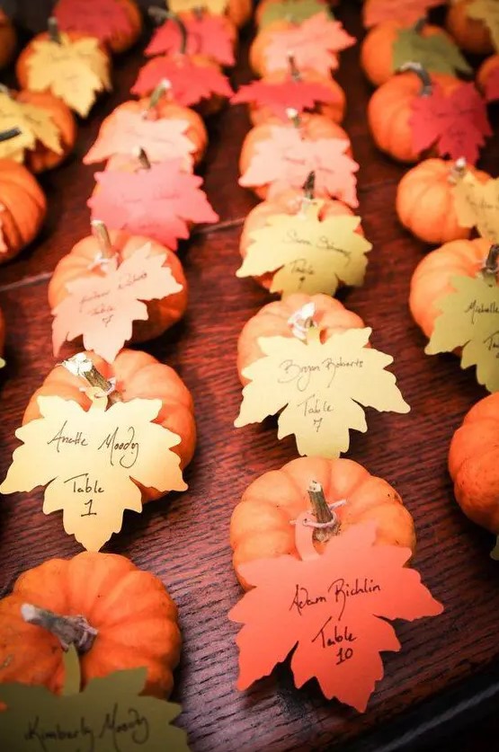 small pumpkins with escort cards shaped as leaves are a cool idea for a fall wedding, they can double as guest favors