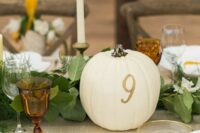 stylish modern fall wedding table decor with foliage, a white pumpkin with a number, candles, brown glasses and vintage cutlery