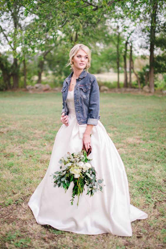 a blue denim jacket with rolled up sleeves over a modern wedding ball gown is a cool outfit for a casual bride