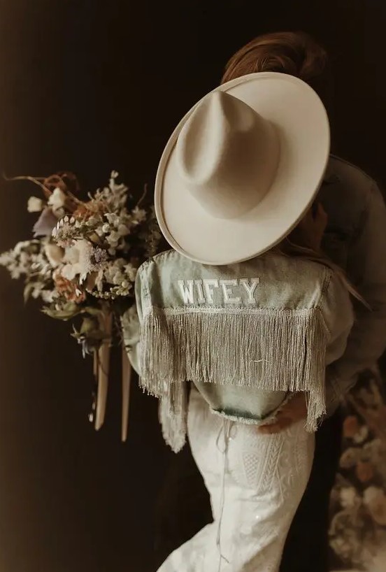 a bleached denim jacket with letter applique and silver fringe, a neutral hat are perfect accessories for a boho bride