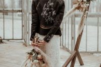 a boho bridal look with a boho lace wedding dress, a black leather jacket with a quote and a boho wedding bouquet with pampas grass