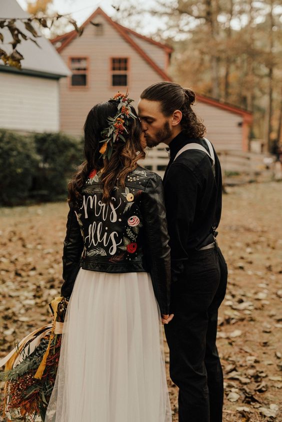 a chic bridal look with a neutral wedding dress, a black leather painted jacket and a bold floral crown is wow