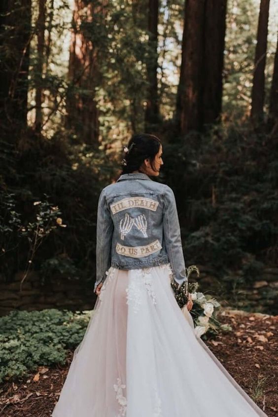 a customized blue denim bridal jacket with letters and skeleton hands is a cool cover up for a wedding