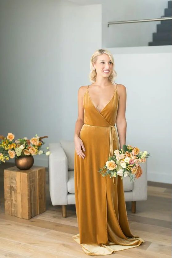 an elegant marigold velvet wrap spaghetti strap bridesmaid dress with a train and a matching bouquet for a fall wedding