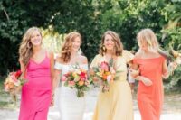 colorful maxi bridesmaid dresses – a pink, yellow and orange one, with mismatching looks are cool for a tropical wedding