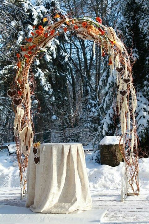frosted outdoor winter arch with orange flowers and fabric hearts hanging