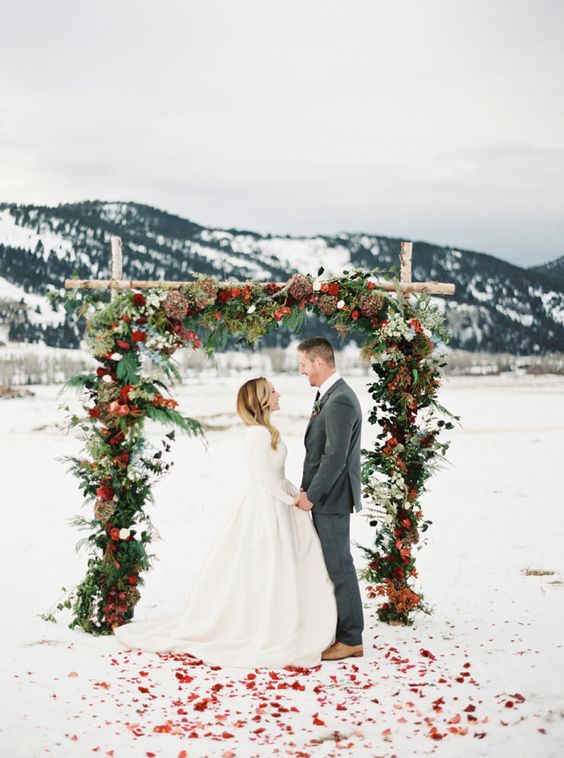gorgeous outdoor wedding arch with leaves, fir, bold blooms and fruit