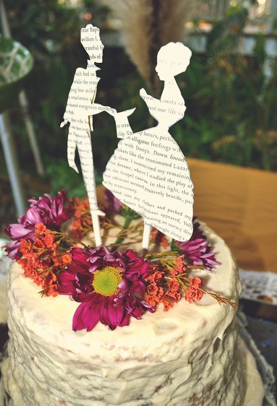 wedding cake topped with fresh flowers and cutout silhouettes from book pages
