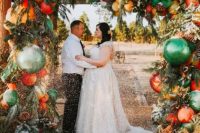 a Christmas wedding arch decorated with evergreens, pinecones, bold green, red, yellow ornaments and with glitter is an ultimate idea