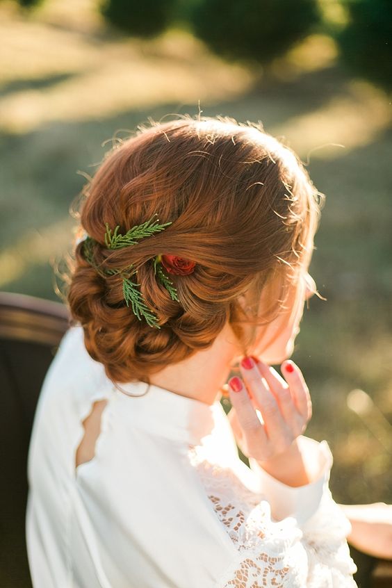A beautiful and eye catching copper braided and woven updo with greenery and a red rose is a stylish idea for a Christmas wedding