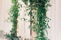 a beautiful and super lush greenery wedding arch and floating candles in glasses around is a very cool and fresh idea for a modern wedding