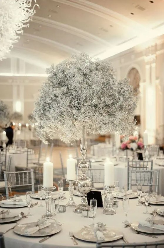 a beautiful ethereal Christmas wedding centerpiece of a baby's breath ball on a tall stand and candles around looks frozen
