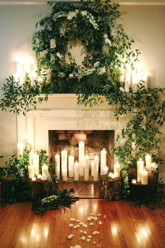 a beautiful fireplace with candles inside, around and on the mantel, with lush greenery and white blooms