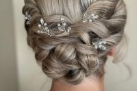 a braided woven low updo with a bump and some rhinestone hair pins is a chic and stylish idea for a bride