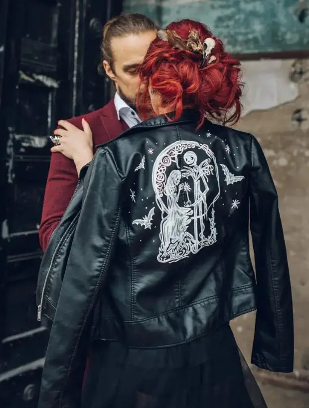 a bride wearing a black wedding dress and a black leather jacket with Tim Burton movie characters painted to personalize it