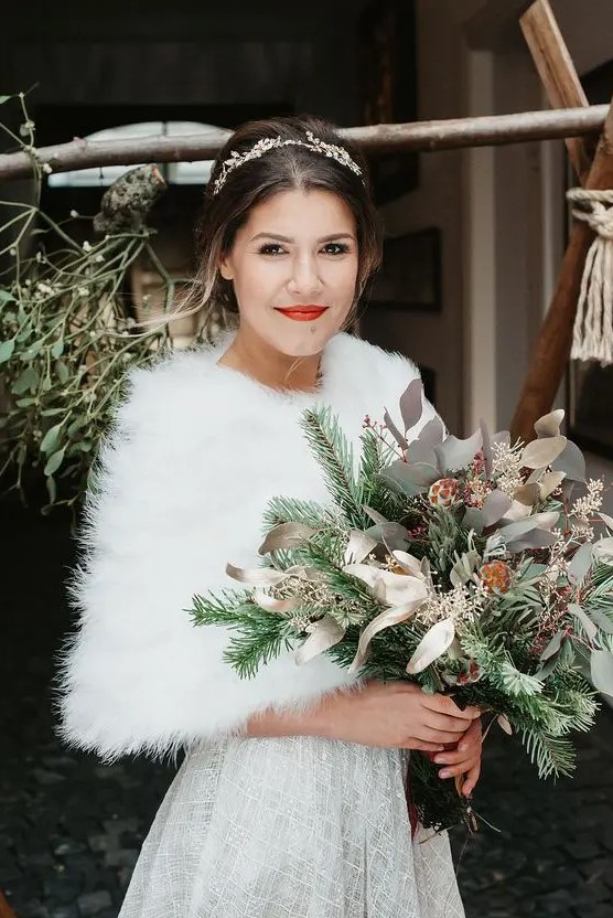 a chic embellished A-line wedding dress paired up with a white faux fur cover up and an embellished hairpiece for a Christmas bridal look