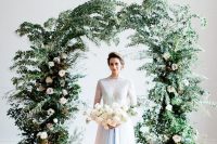 a chic winter wedding arch with greenery and blush roses plus candles around is a cool idea for both indoors and outdoors