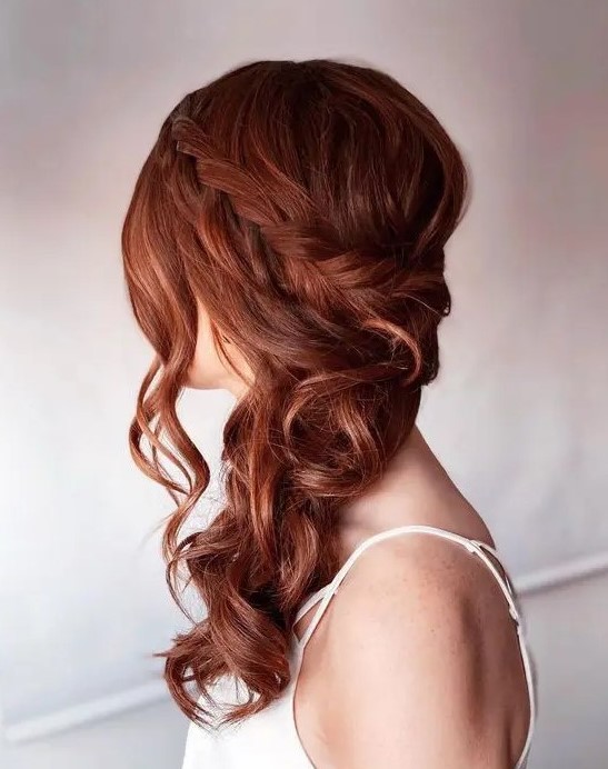 a classy and chic ginger side swept hairstyle with a braided halo, wavy hair down and some waves framing the face