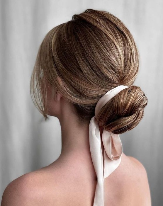 A classy wrapped low bun with a bump on top, a silk ribbon and face framing locks is a chic and stylish idea