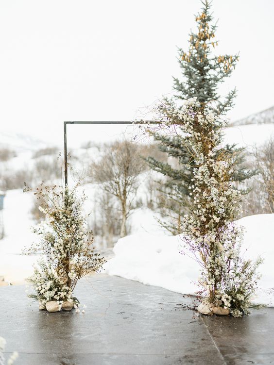 a cool frozen winter wedding arch decorated with white blooms and berries on twigs and branches is a cool idea for an outdoor wedding