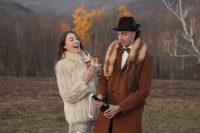 a creative boho groom’s look with a rust-colored coat with a fur collar, black trousers, brown shoes and a brown bow tie